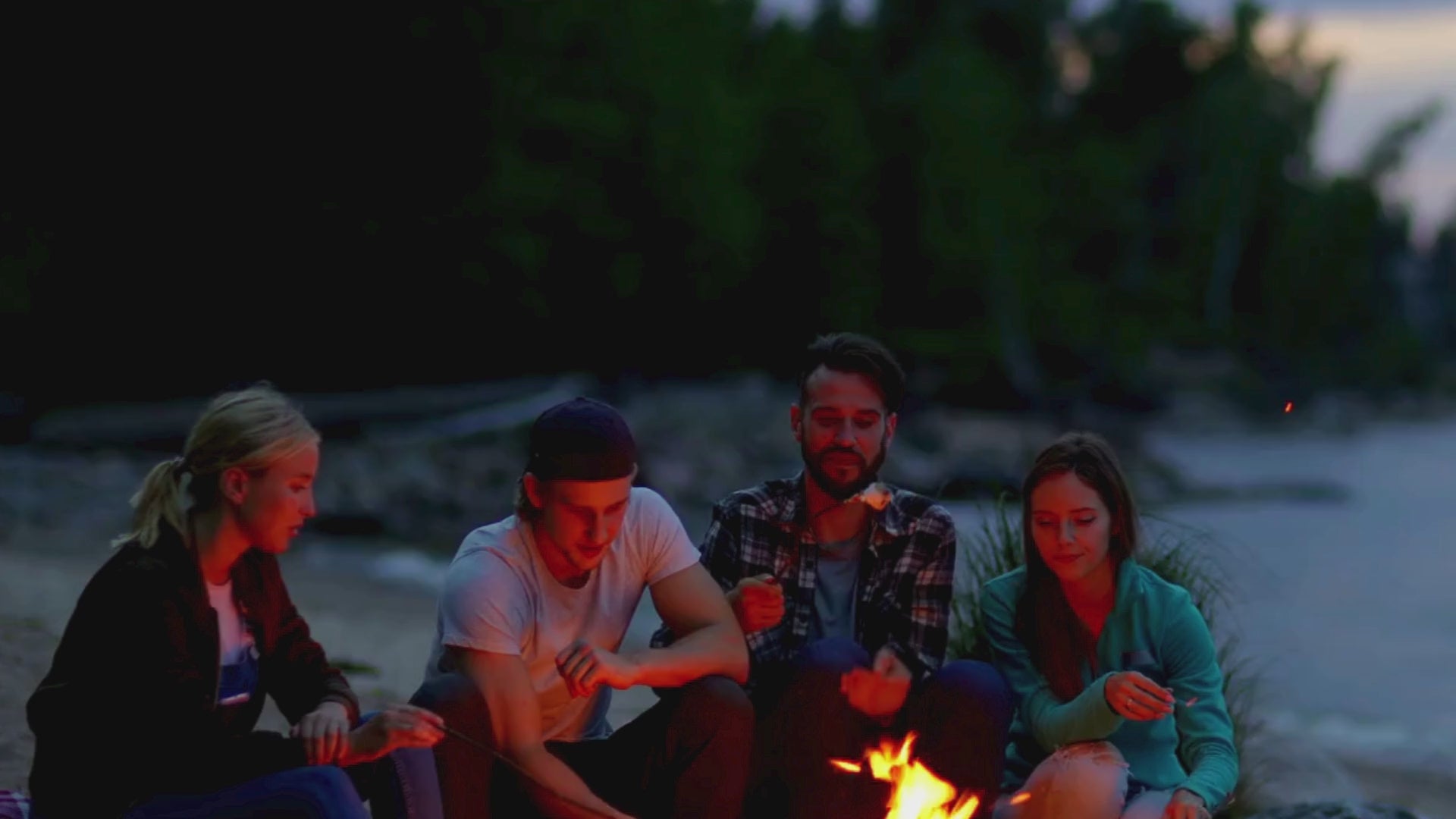 Video laden: Vier Freunde rösten Marshmallows am Lagerfeuer in fröhlicher Stimmung, kein Ton.